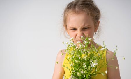 Dissatisfied capricious little girl screwing up her face looking on a bouquet of field flowers in her hands. Children, gesturing and emotions, unhappy with a gift. Close up portrait isolated on whiteの写真素材