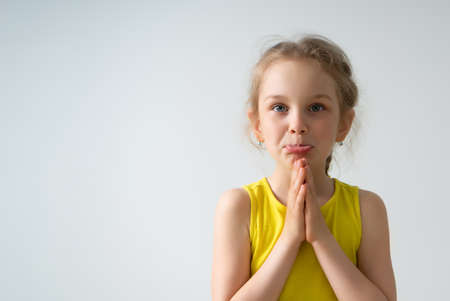 Cute girl preschooler is begging to buy or to give her something folding palms together and pushing her lower lip out. Children, gesturing and emotions. Cropped shot isolated on white, copy spaceの写真素材