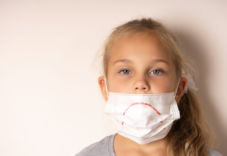 Sad girl in a medical mask. She painted a sad smile on the mask.の写真素材