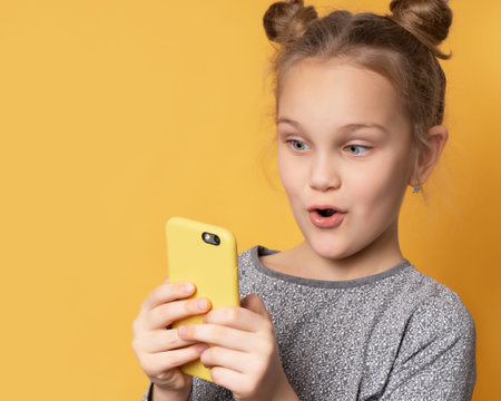 Portrait of excited beautiful girl playing games on mobile phone isolated on yellow background