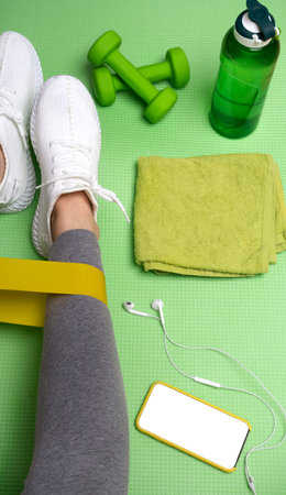top view of a woman preparing for a sports workout with a dumbbell and an elastic band. Sports at...