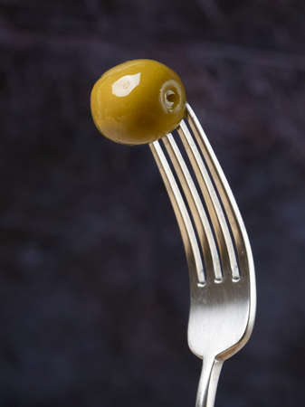 one green olive on a fork isolated on blue backgroundの写真素材