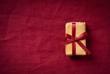 gift box in craft paper on a burgundy linen fabric background. top view, place for your text, postcard.の写真素材