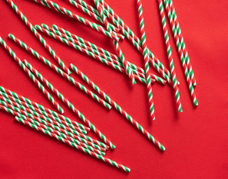 Striped red-green-white paper cocktail tubes on a red fabric background.の写真素材