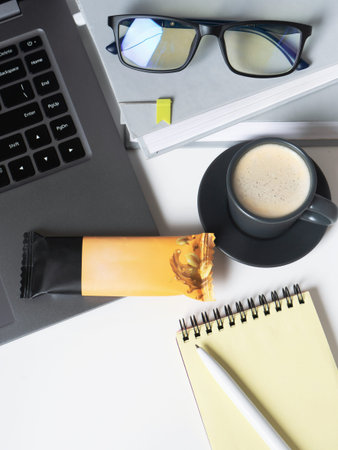 snack at work. Top view of workplace desk with laptop, cup of coffee, glasses, notepad and protein...