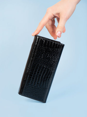 light touch of a womens patent leather wallet on a blue background.
