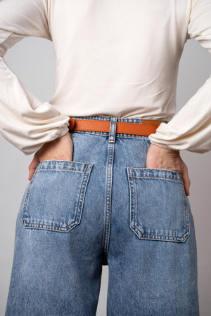 Woman in casual wear with white blouse, blue vintage high waist mom jeans, red belt on gray...