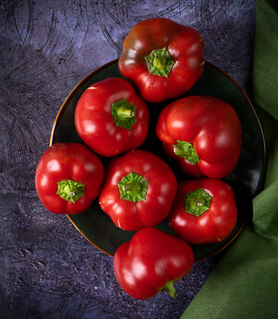 several red peppers of the Bulgarian sweet round variety on a ceramic plate on a dark black backgroundの写真素材