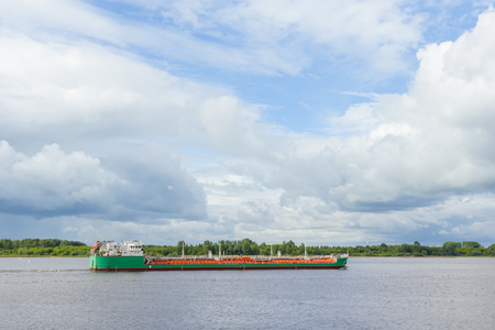 A green tanker is walking along the river at summerの写真素材