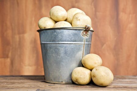 Old bucket filled with potatoes against a rustic backgroundの写真素材