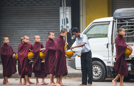 MARCH 07 , 2017: Buddhist monk in brown robe waking in line and receiving alms giving from the people in morning near Shwedagon pagodaのeditorial素材