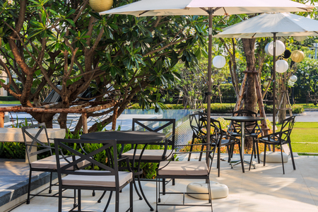 Cafe tables and chairs outside with big white umbrella and poolの写真素材