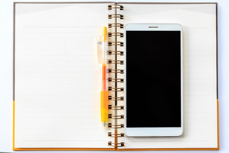 Yellow pen on a notebook and white cell phone on white background.の写真素材