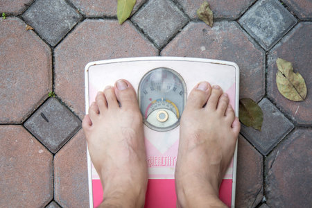 Asian Men's Foot on a old pink weighing apparatus on brick paving