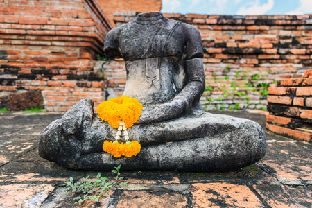 A marigold garlan on the hand of statue buddha with old brick wall background in The Historical Park of Ayutthaya,The favorite historical attractions of Ayuttaya Thailand.の写真素材