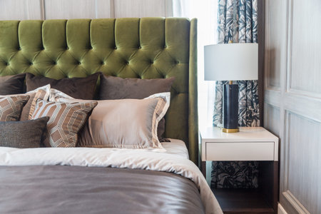 A white lamp side the bed with a brown pillows learning green headboard with a warm light from a...