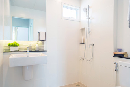tiwith a white ceramic basin and a mirror with a shower on a white wall.の写真素材