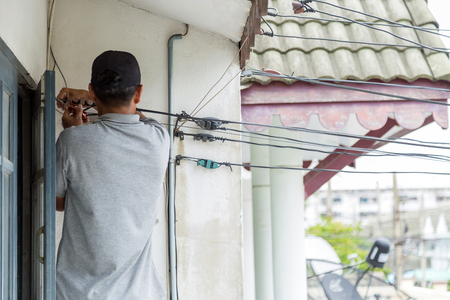 The asian technician man are installing internet cable to wire holder at wall into hame, selective focus on hands rolling internet cable. The asian technician man are installing internet cable to wire holder at wall into hame, selective focus on hands rolling internet cable.