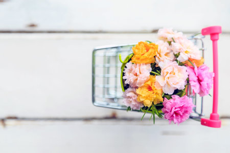 A beautiful bouquet moss rose flowers in a mini green bucket in mini shopping cart on wooden floor...