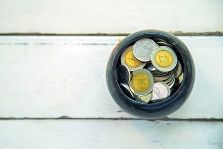 Top view of coins in wooden bowl on white wooden table with sunlight. saving money concept.の写真素材