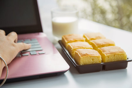 Close up a butter cake pack in a brown plastic box next to a pink laptop device with a woman hand...