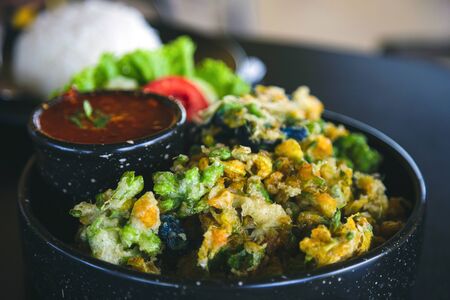 Crispy Vegetable Fritters in a black plate with Thai chili sauce on a black table with rice blurred background, Thai food concept.の写真素材