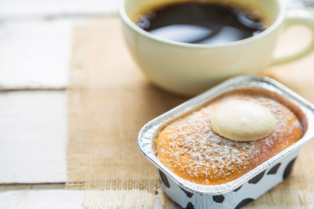 Close up a cup of Dalgona coffee with coffee beans next to a glass window on a white table with a...