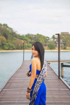 Portrait Asian woman in blue casual wear with a sunglasses, she is standing on a wooden bridge with a sea background.の写真素材