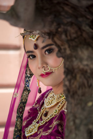 Portrait Asian woman in a margenta Indian tradition sari, she is hide her face by tree and looking at a cameraの写真素材