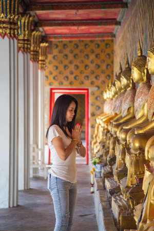 Asian woman in a white t-shirt to pay respect to Buddha statue in the Buddhist temple while traveling in Wat Arun temple Thailandの写真素材