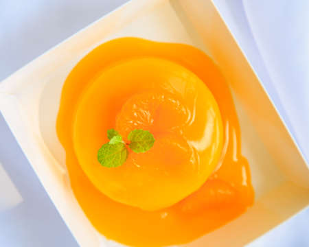 An orange cake with orange topping and pepermint on a white table.の写真素材