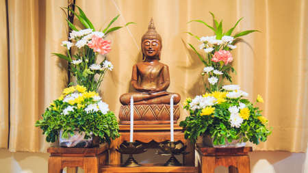 A wooden Buddha image in the posture of meditating on a altar table topped with flowers.の写真素材