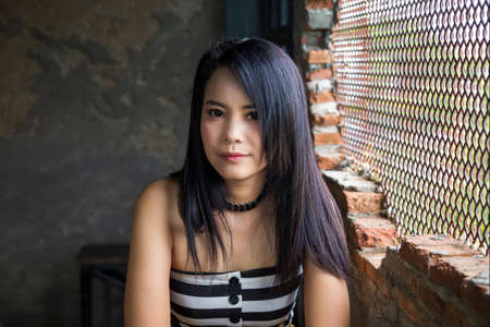 Portrait Asian woman lookinging at a camera next to brick wall.の写真素材