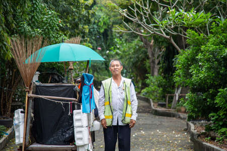Portrait happy old Asian man street cleaner standing next to an old gabage cart before going to work with nature background.の写真素材