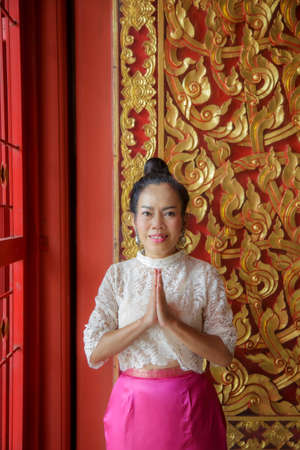 Portrait of Thai mature women in a white shirt pay respect in front of a beautifully carved wooden door.の写真素材
