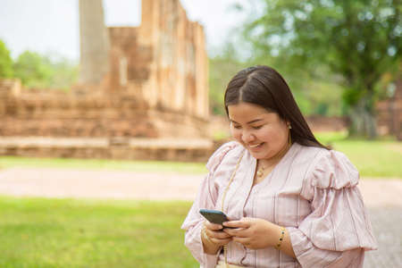 Smiling chubby Asian woman using a cell phone while traveling in a Buddhist temple in Asia.の写真素材