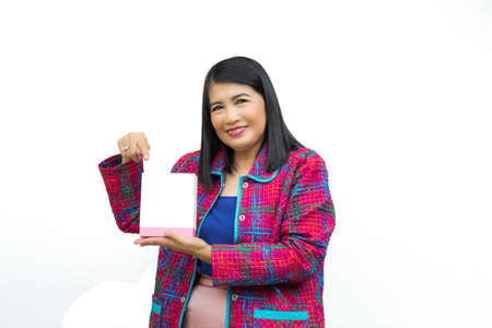 Close up cnfident middle-aged Asian woman wearing pink casual wear holding and pointing a white box on her hand on white background.の写真素材