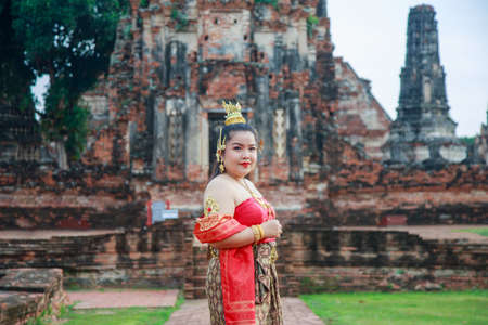 Asian woman in a Thai traditional dress posing in front of an ancient structureの写真素材