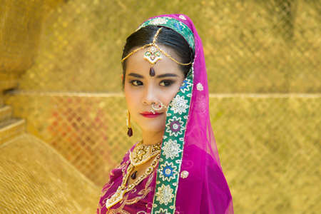 Portrait Asian woman in a margenta Indian tradition sari, she is looking at a camera next to the an orange wallの写真素材