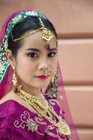 Portrait Asian woman in a margenta Indian tradition sari, she is looking at a camera next to the an orange wallの写真素材
