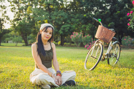 Portrait Asian woman in a green singlet sitting on a bicycle on a lawn with nature background in a parkの写真素材
