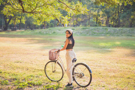 Portrait Asian woman in a green singlet sitting on a bicycle on a lawn with nature background in a parkの写真素材