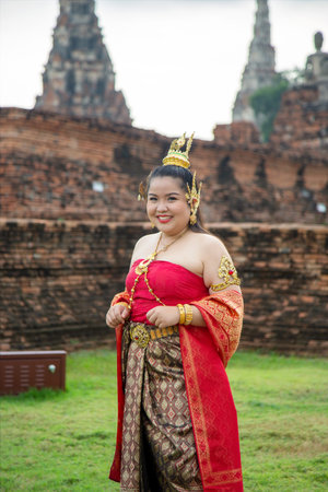 Asian woman in a Thai traditional dress walk to an old brick gate with a big root tree cover wallの写真素材