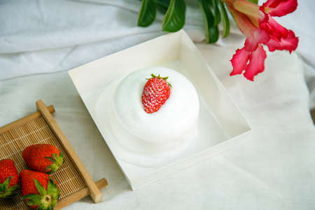 A cup of cake with strawberry fruit on top in a paper box on a white tableの写真素材