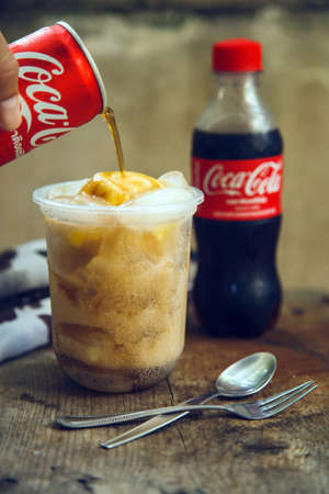 Bangkok ,Thailand - 2022 March 28 : A Man hand pouring Coke on vanilla ice cream in glass on the wooden tableのeditorial素材