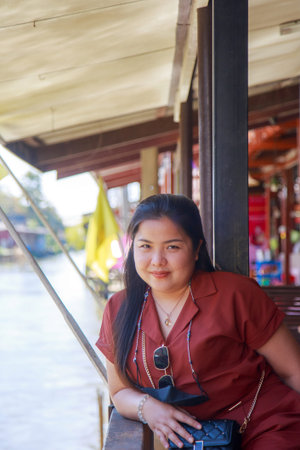 Portrait Asian woman in a pink shirt looking at side, she is sitting on waterfront terrace with canal backgroundの写真素材