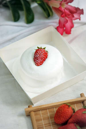 A cup of cake with strawberry fruit on top in a paper box on a white tableの写真素材