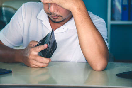 Close up Serious Asian man in a white shirt put his forehead on his hand watching a wallet at the officeの写真素材