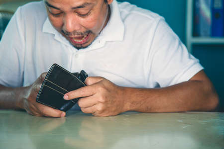Close up Serious Asian man in a white shirt put his forehead on his hand watching a wallet at the officeの写真素材