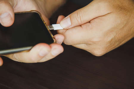 Close up a man's hands using a USB type C cable to charge a mobile phone on a wooden tableの写真素材
